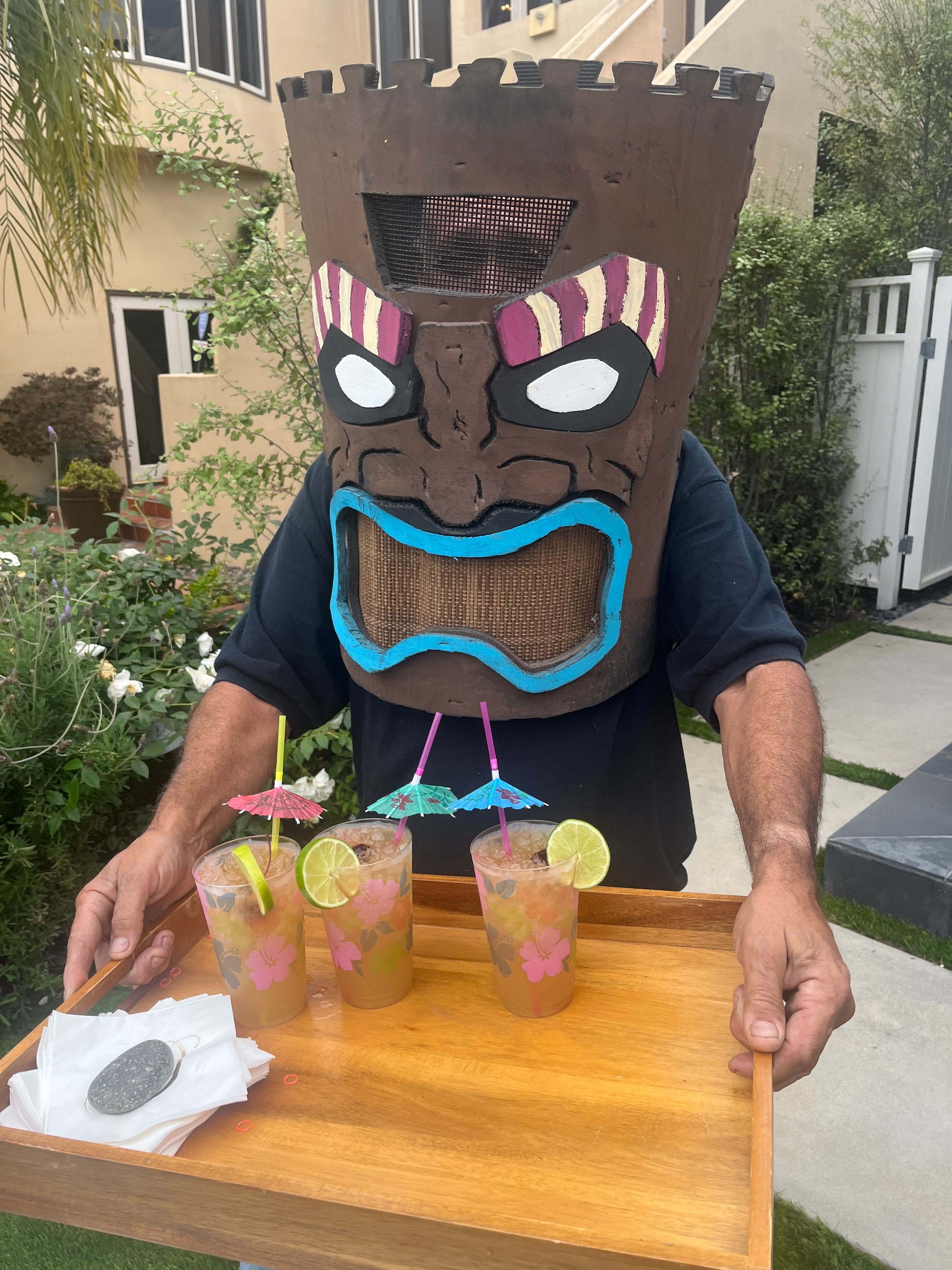 Roaming Tiki costume character holding a tray of tropical mocktail drinks at a backyard event